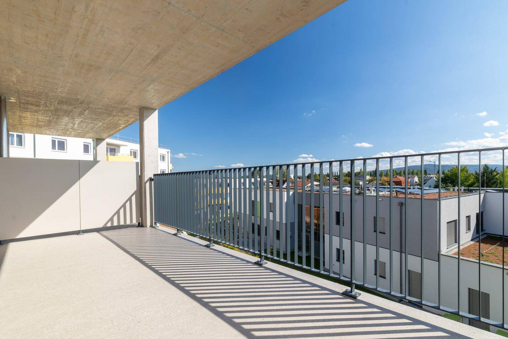Heller Balkon mit modernem Geländer und sonnigem Ausblick auf die Nachbarschaft.