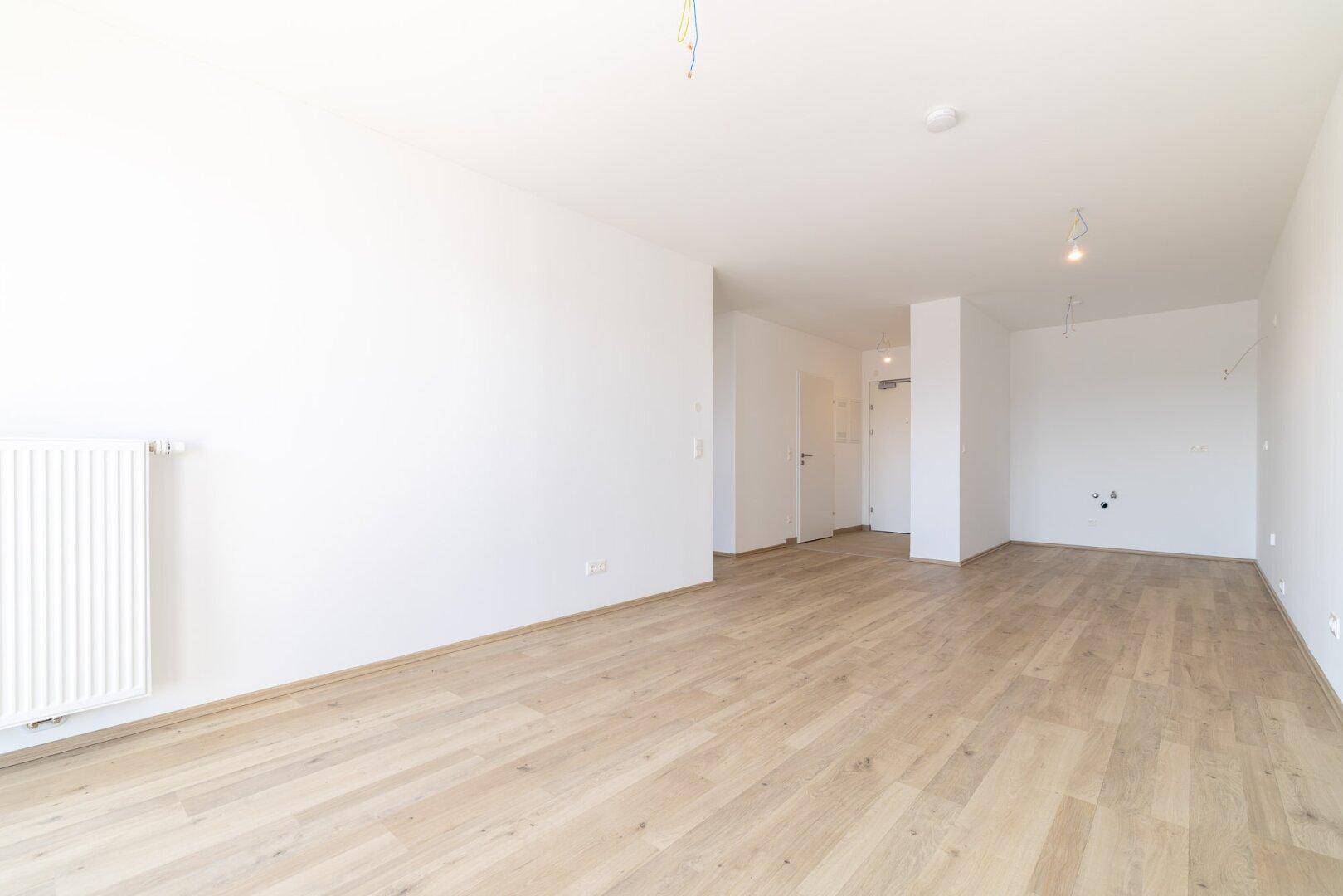 Geräumiger, unmöblierter Raum mit Laminatboden und Heizkörper an der Wand.