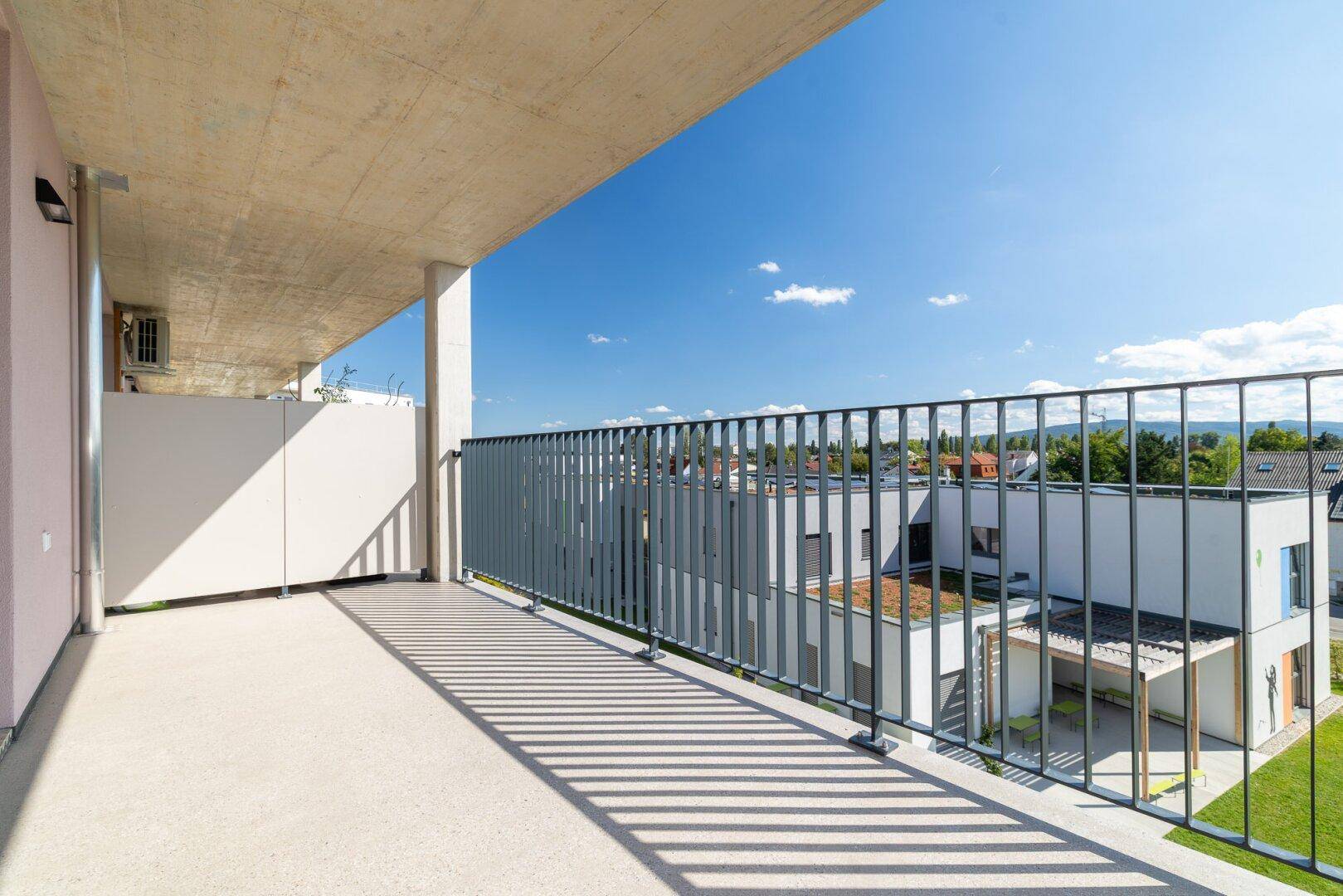 Langer Balkon mit schlichtem Design und Blick auf die umliegenden Gebäude und Grünflächen.