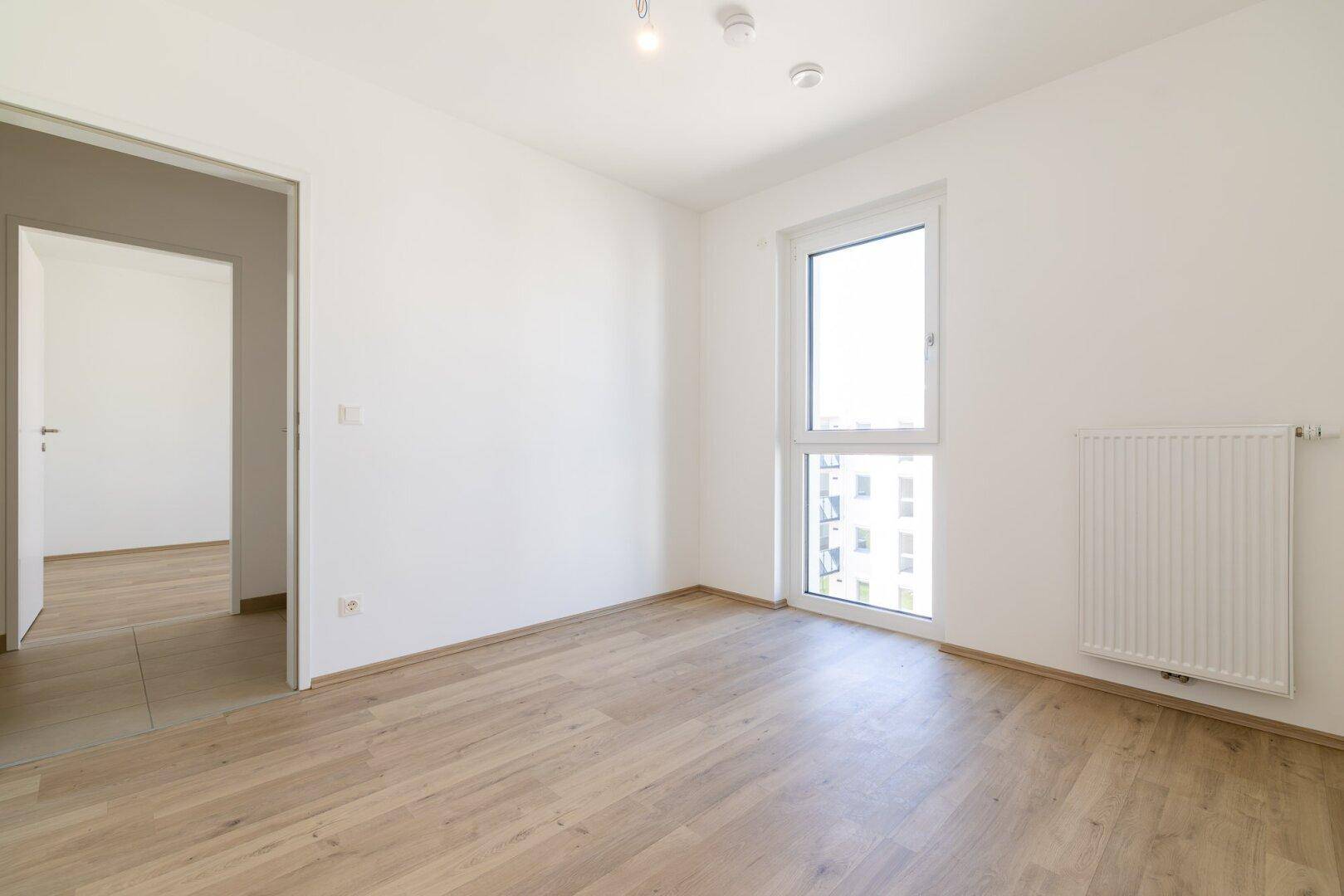Helles, unmöbliertes Schlafzimmer mit Laminatboden und einem großen Fenster.