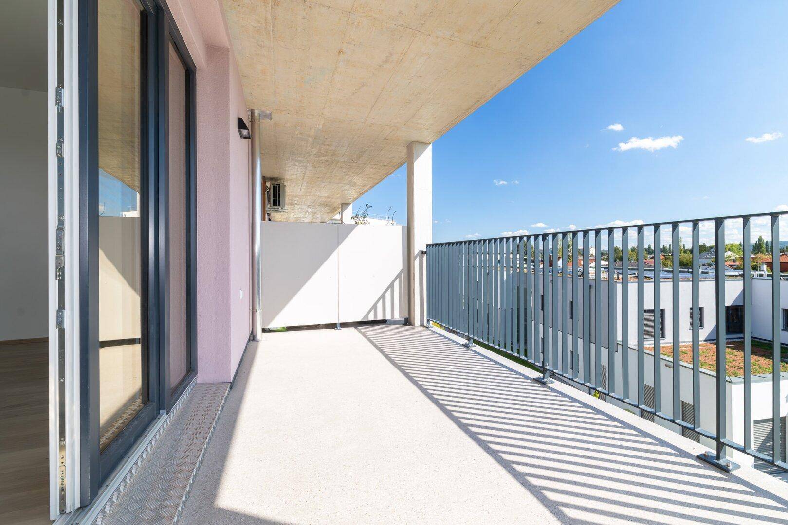 Moderner Balkon mit Betonboden und Metallgeländer, angrenzend an große Glastüren.