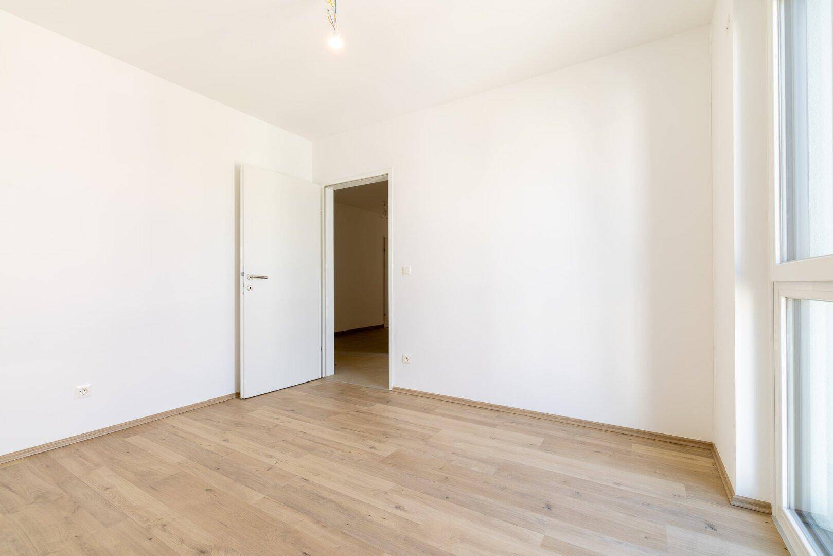 Leeres Schlafzimmer mit hellem Laminatboden und einer weißen Tür, bereit zur Einrichtung.