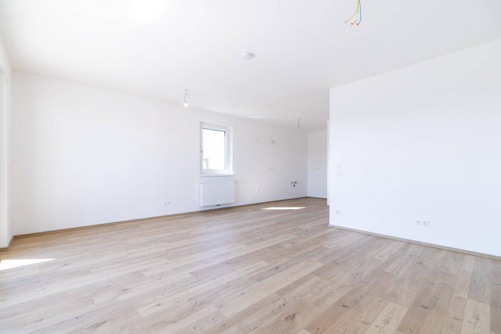 Heller, leerer Raum mit einem Fenster und hellem Laminatboden, bereit zur Einrichtung.