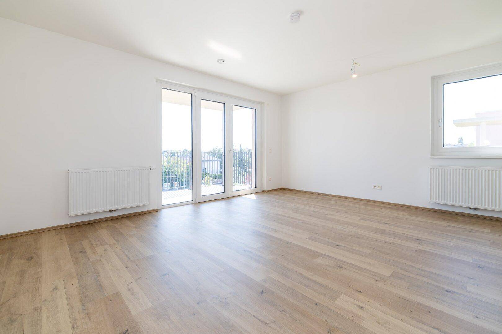 Lichtdurchfluteter, unmöblierter Raum mit großen Fenstern und hellem Laminatboden.