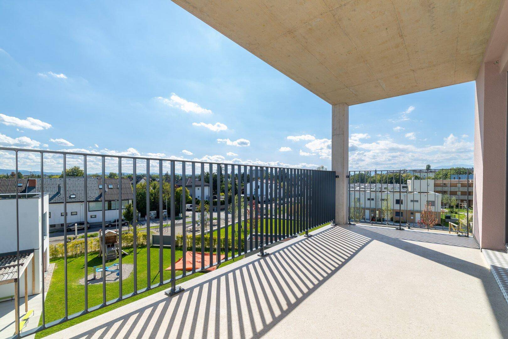 Breiter Balkon mit Metallgeländer und Blick auf eine grüne Wohnanlage.