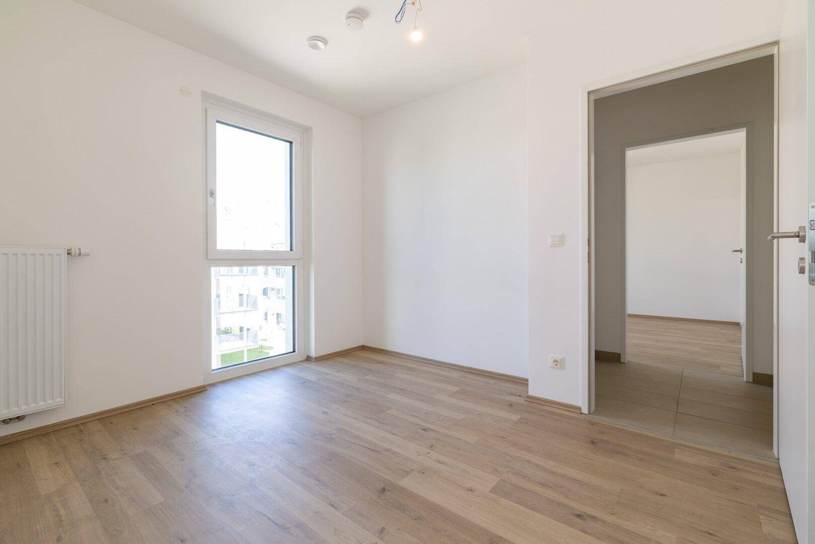 Heller Raum mit Laminatboden und einem Fenster, das einen Blick auf die Umgebung bietet.