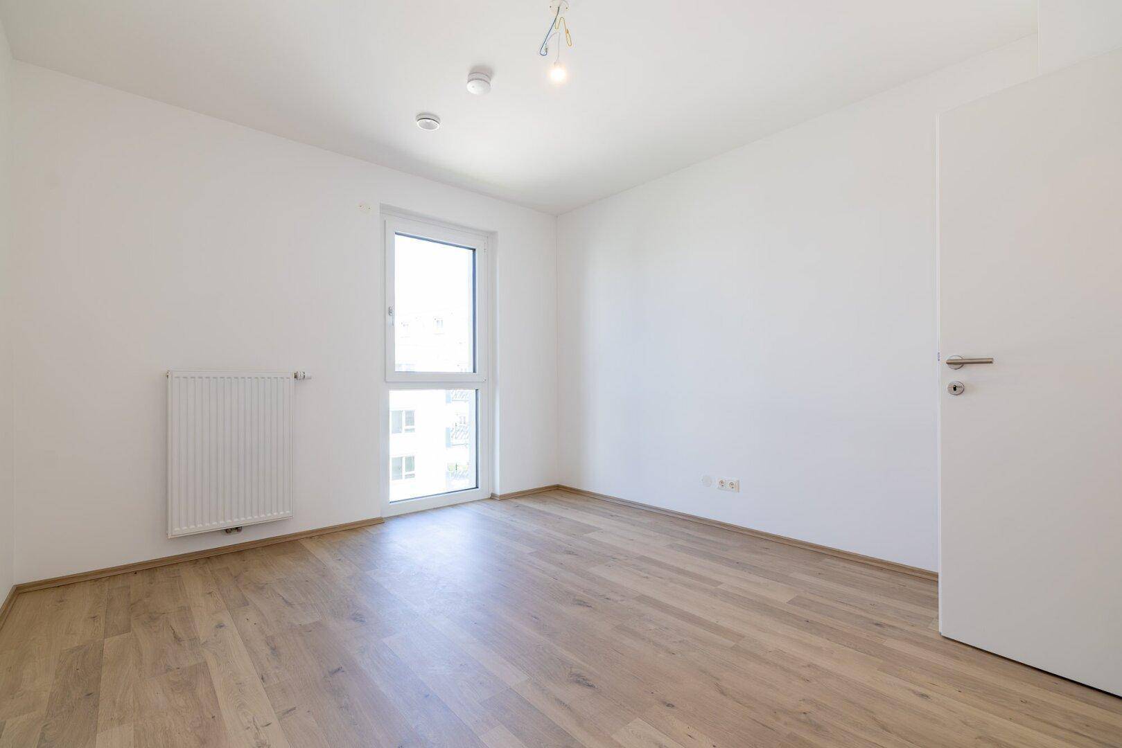 Unmöbliertes Schlafzimmer mit Laminatboden und weißer Tür, bereit für die persönliche Gestaltung.