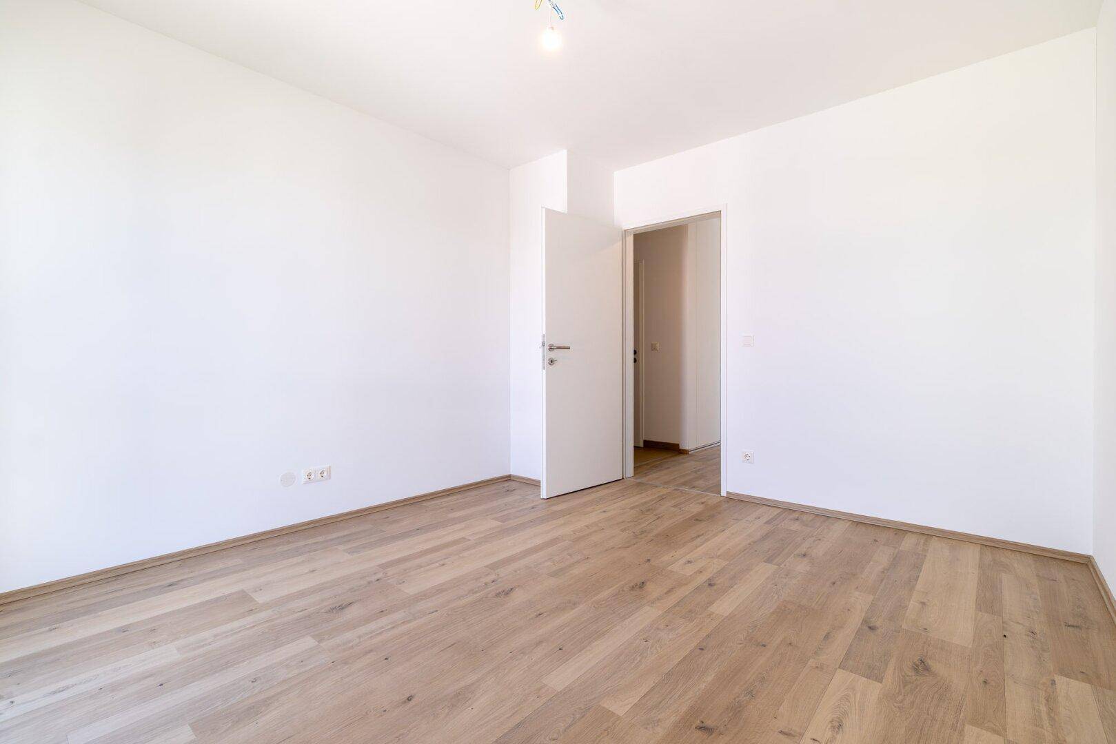 Unmöbliertes Schlafzimmer mit Laminatboden und weiß gestrichenen Wänden, ideal für individuelle Gestaltung.