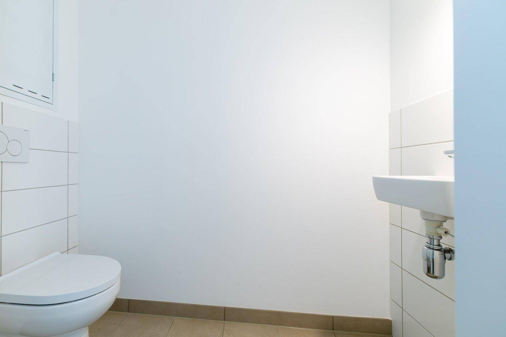 Separates Gäste-WC mit Wand-WC und kleinem Waschbecken, hell gefliest.