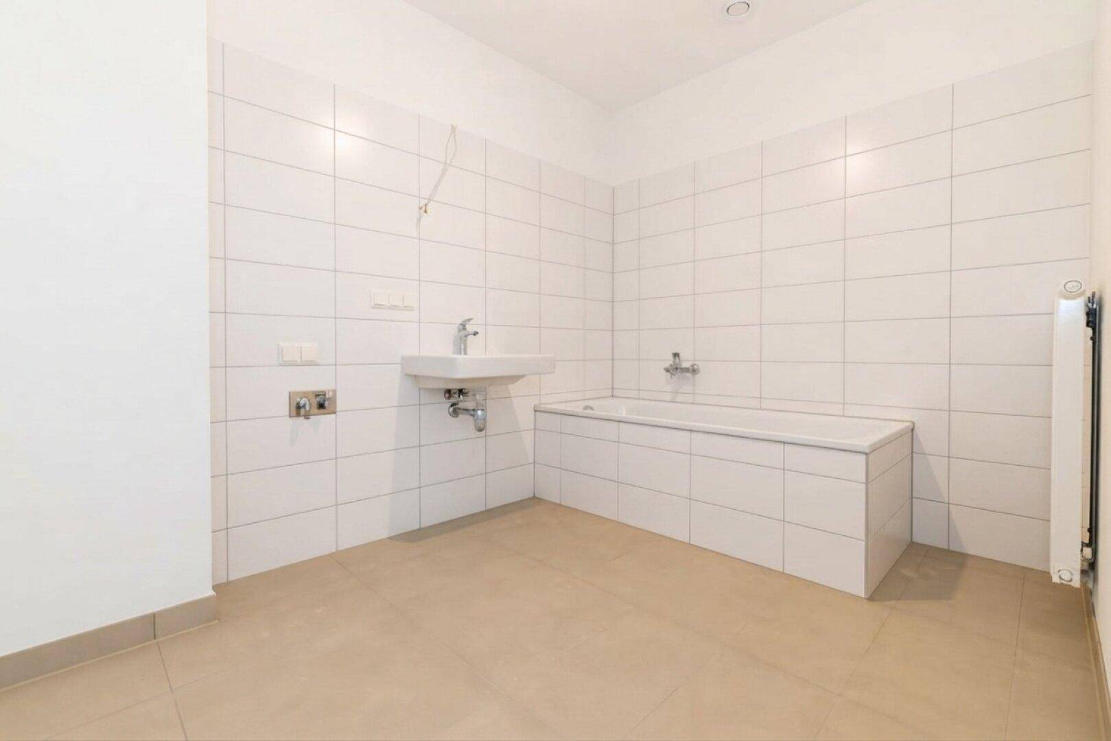 Modernes Badezimmer mit weißen Fliesen, Badewanne und Waschbecken, bereit zur Fertigstellung.