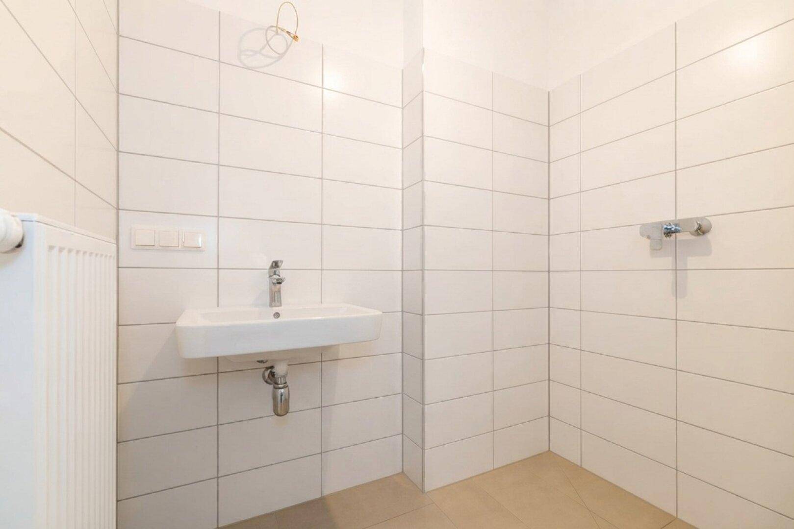 Modernes Badezimmer mit weißen Fliesen, Waschbecken und vorbereitetem Duschbereich.