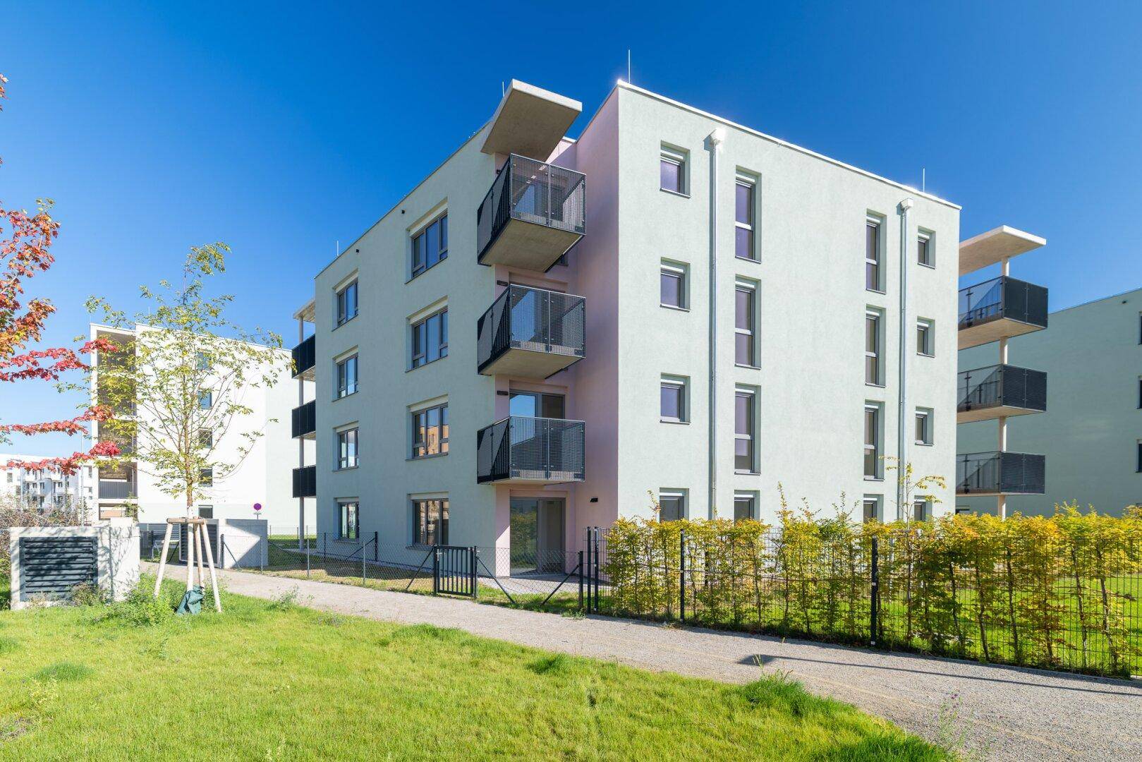 Zeitgenössisches Wohngebäude mit Balkonen und einer gepflegten Hecke in sonniger Umgebung.