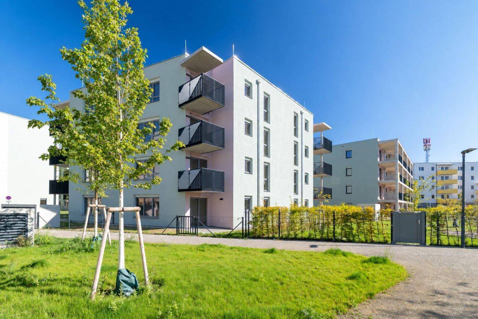 Moderne Wohngebäude mit Balkonen und Grünflächen unter blauem Himmel an einem sonnigen Tag.
