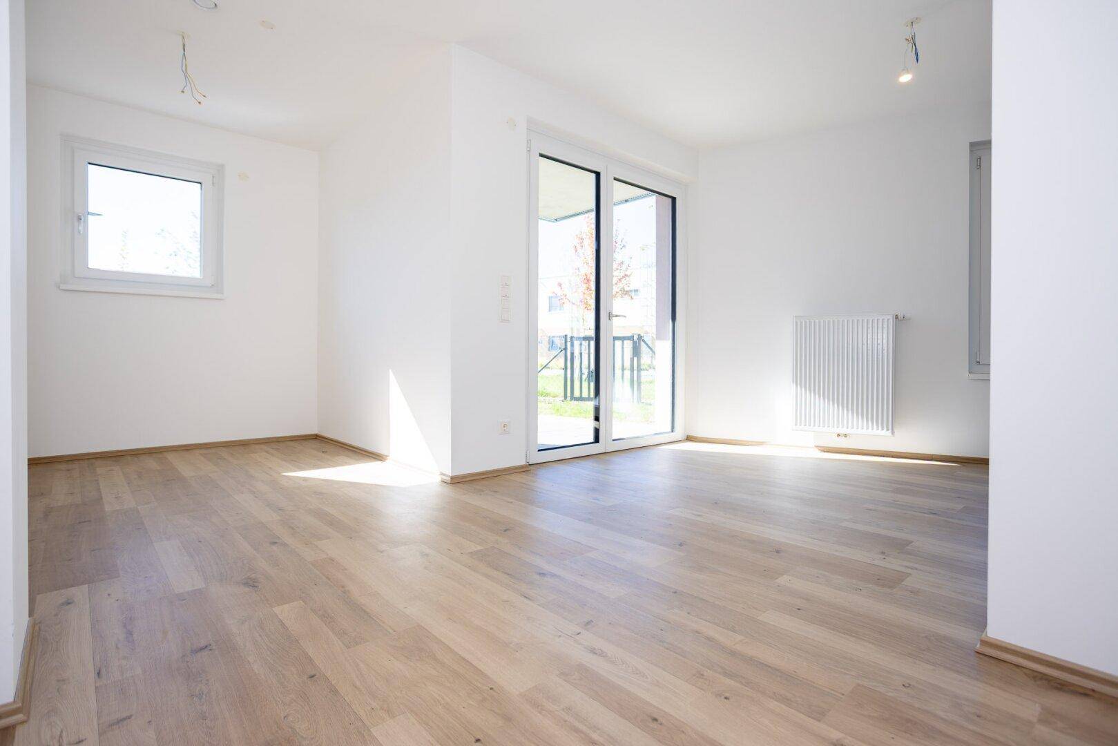 Lichtdurchfluteter Raum mit Laminatboden, weiß gestrichenen Wänden und Zugang nach draußen.