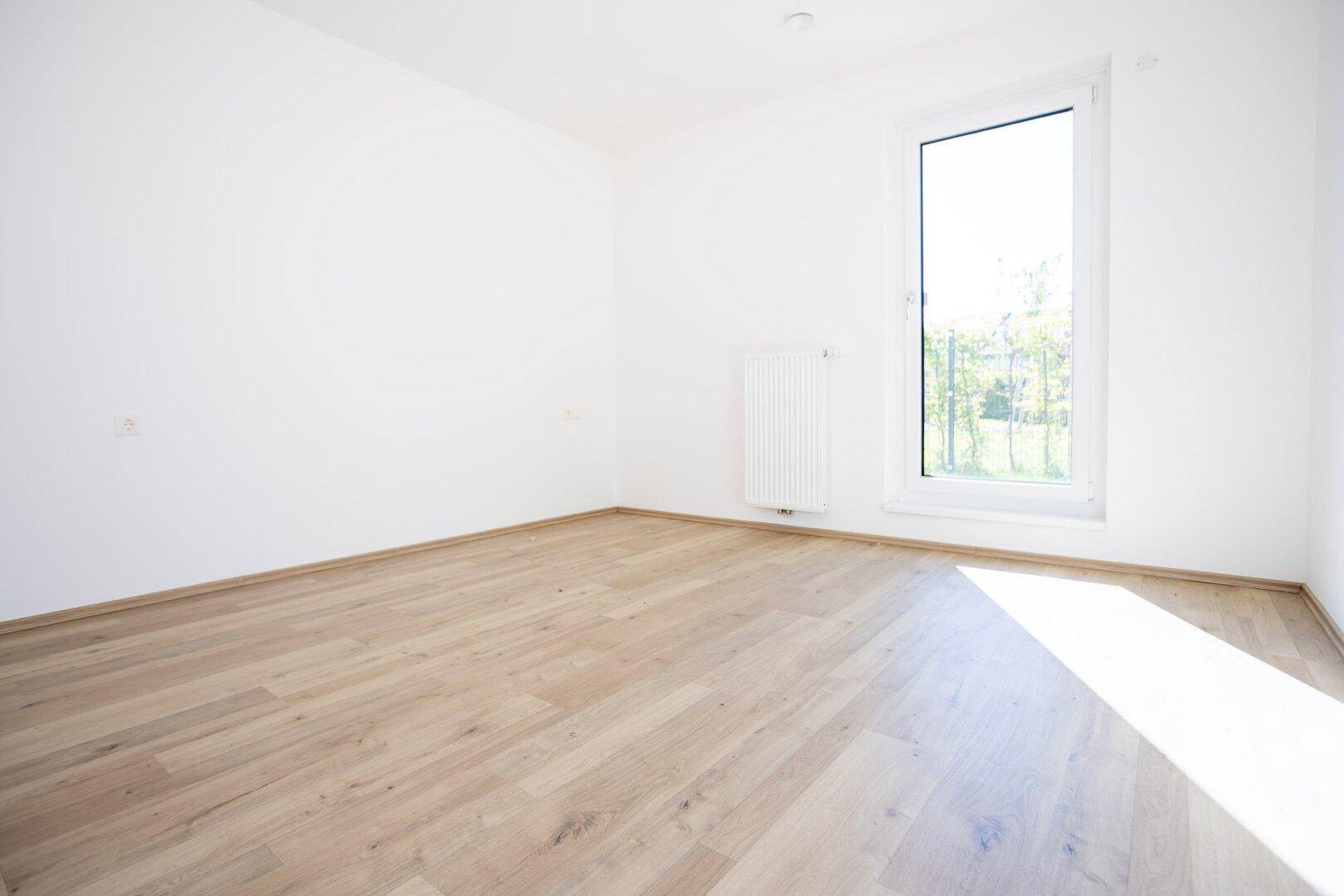 Helles Schlafzimmer mit Laminatboden, großem Fenster und viel Tageslicht.