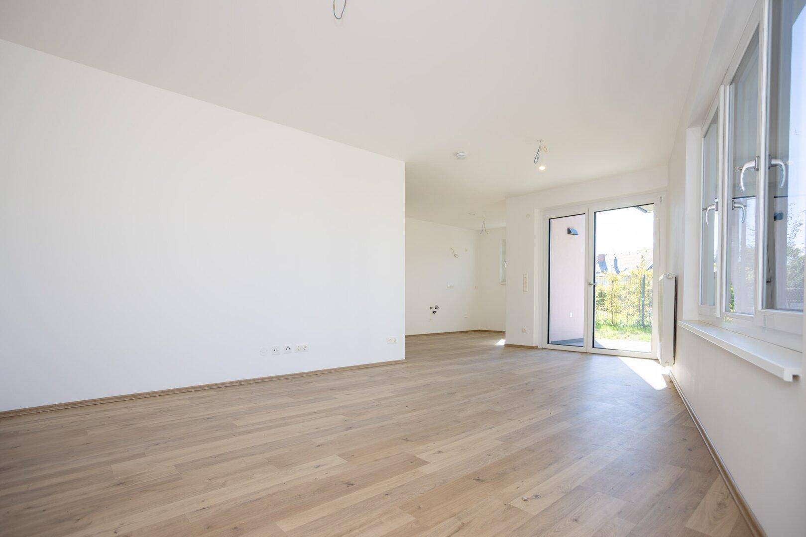 Geräumiges, helles Wohnzimmer mit Laminatboden und großen Fenstern, bereit zum Einzug.