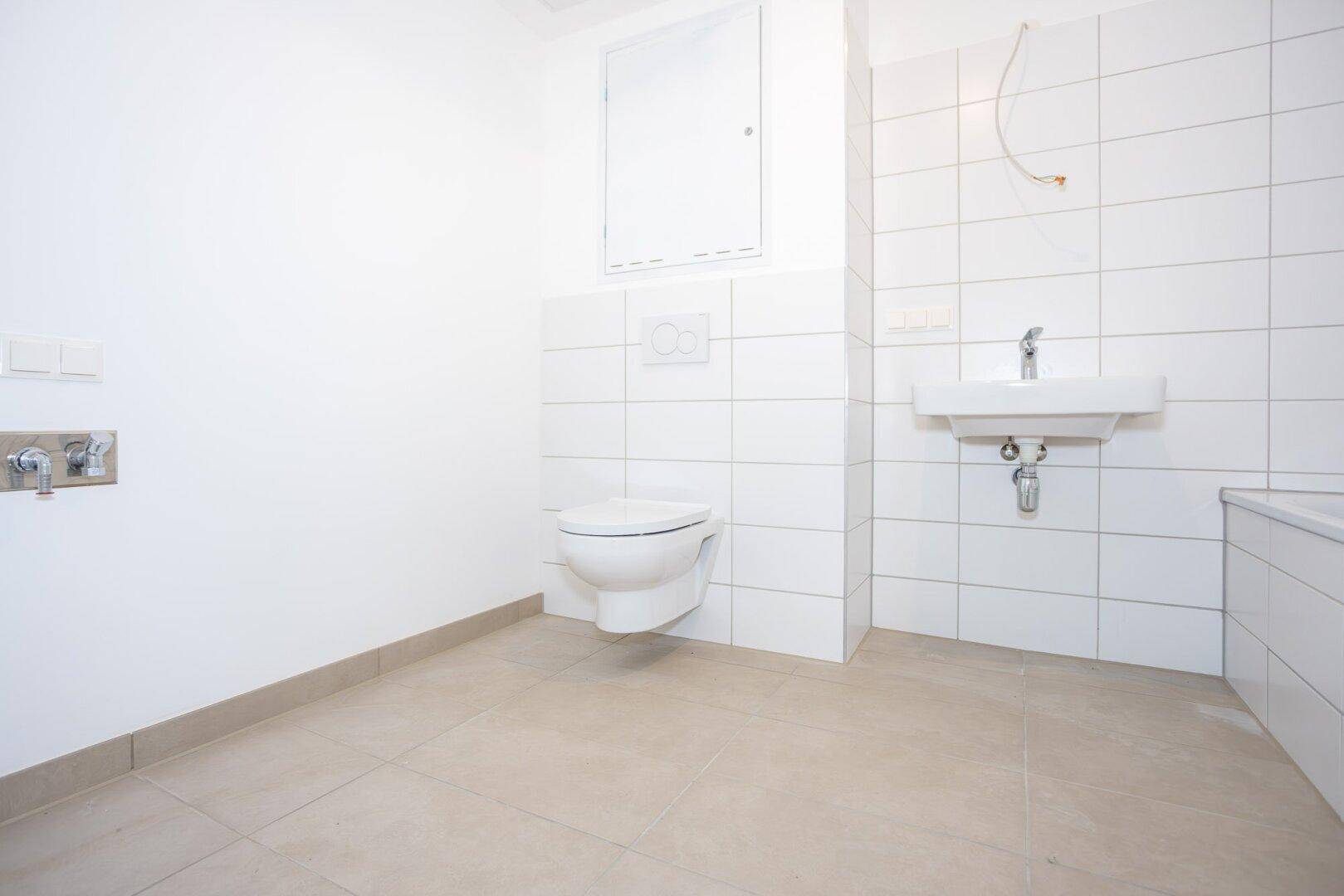 Helles Badezimmer mit weißen Fliesen, wandhängendem WC und Waschbecken.