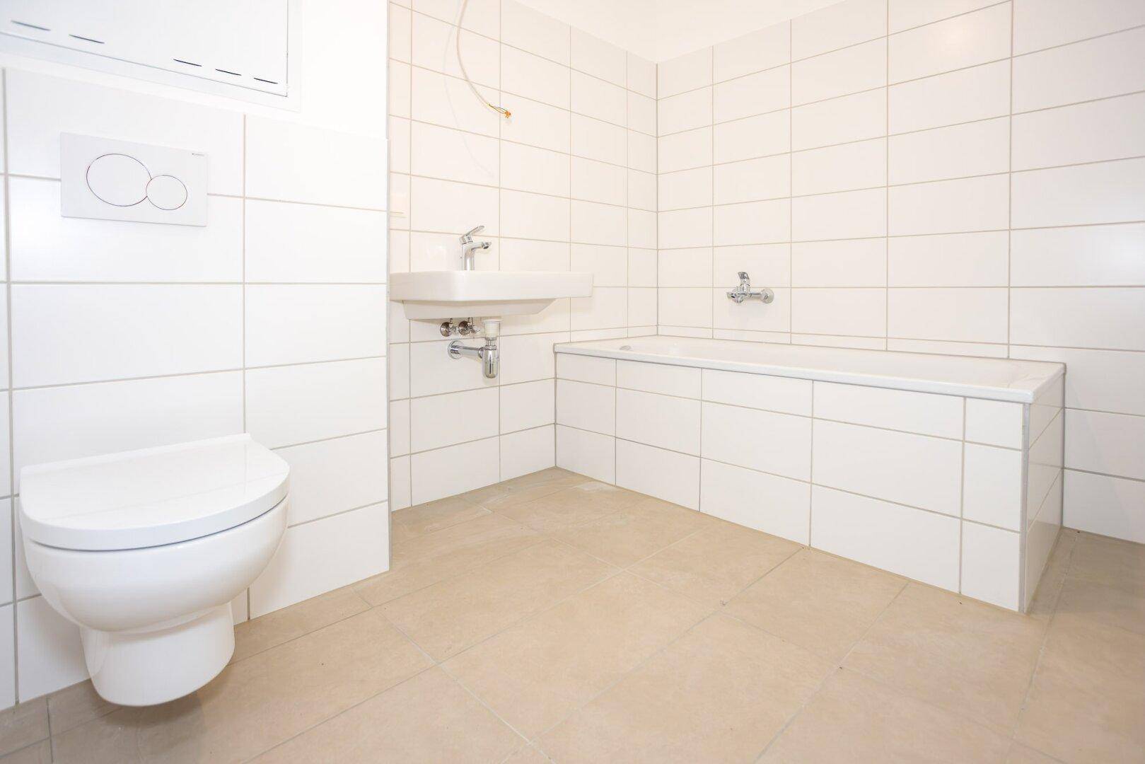 Modernes Badezimmer mit weißen Fliesen, Badewanne und wandhängendem WC.