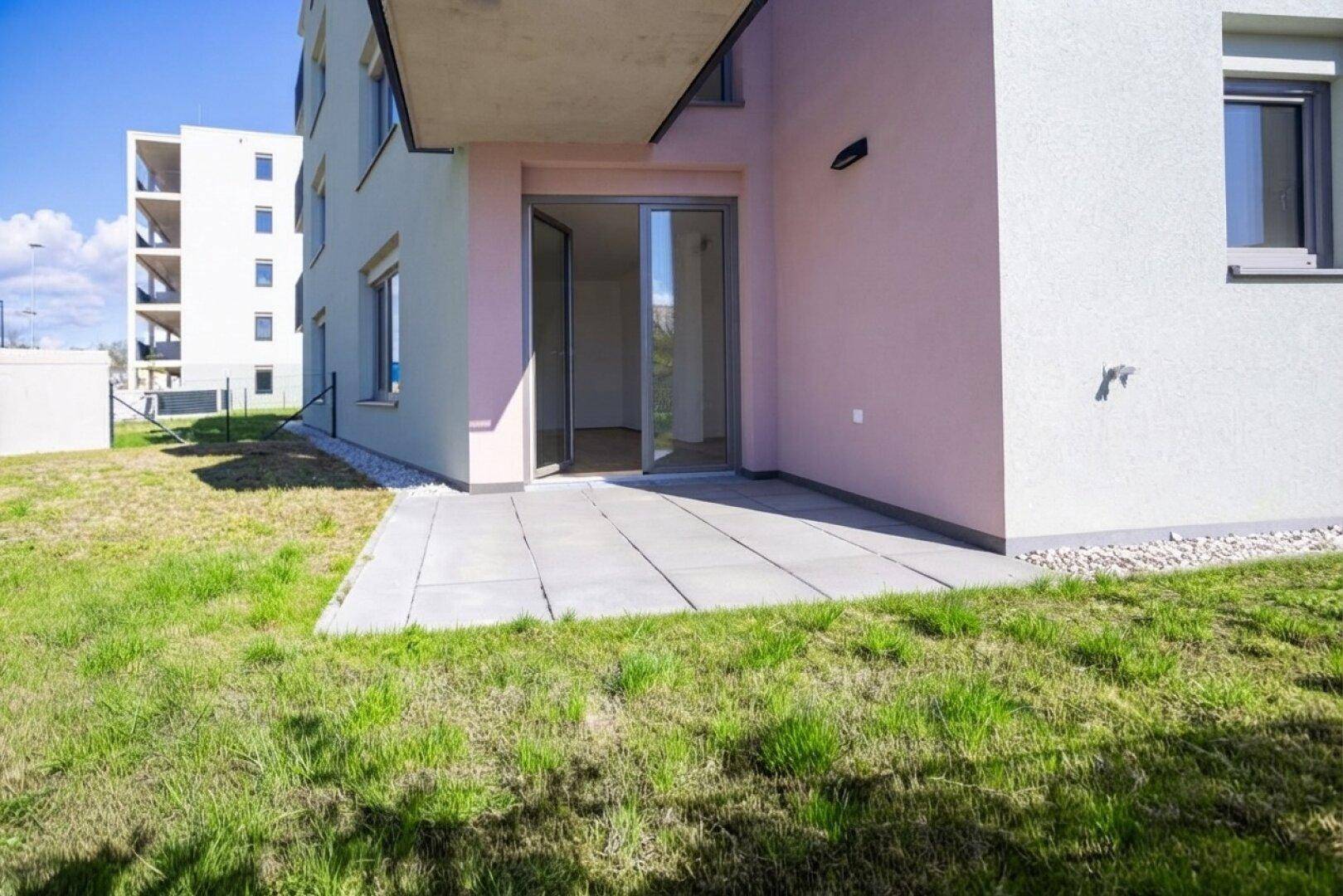 Kleine gepflasterte Terrasse am Gebäude mit Rasenfläche und Blick auf die Umgebung.