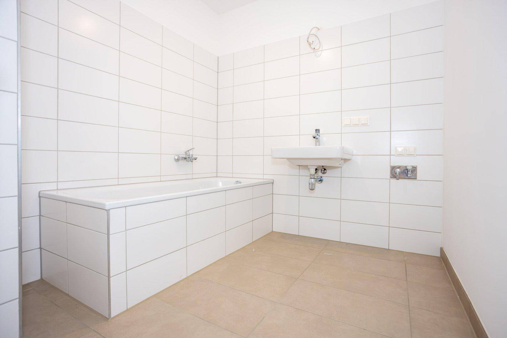 Helles Badezimmer mit Badewanne, Waschbecken und weißen Wandfliesen.