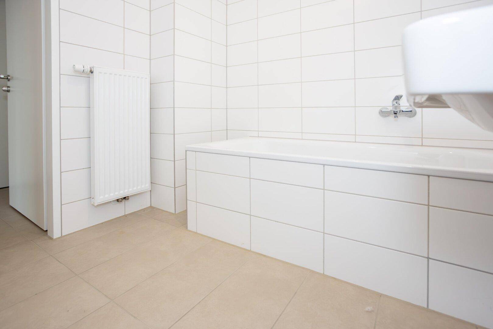 Modernes Badezimmer mit weißen Fliesen, Badewanne und Heizkörper.