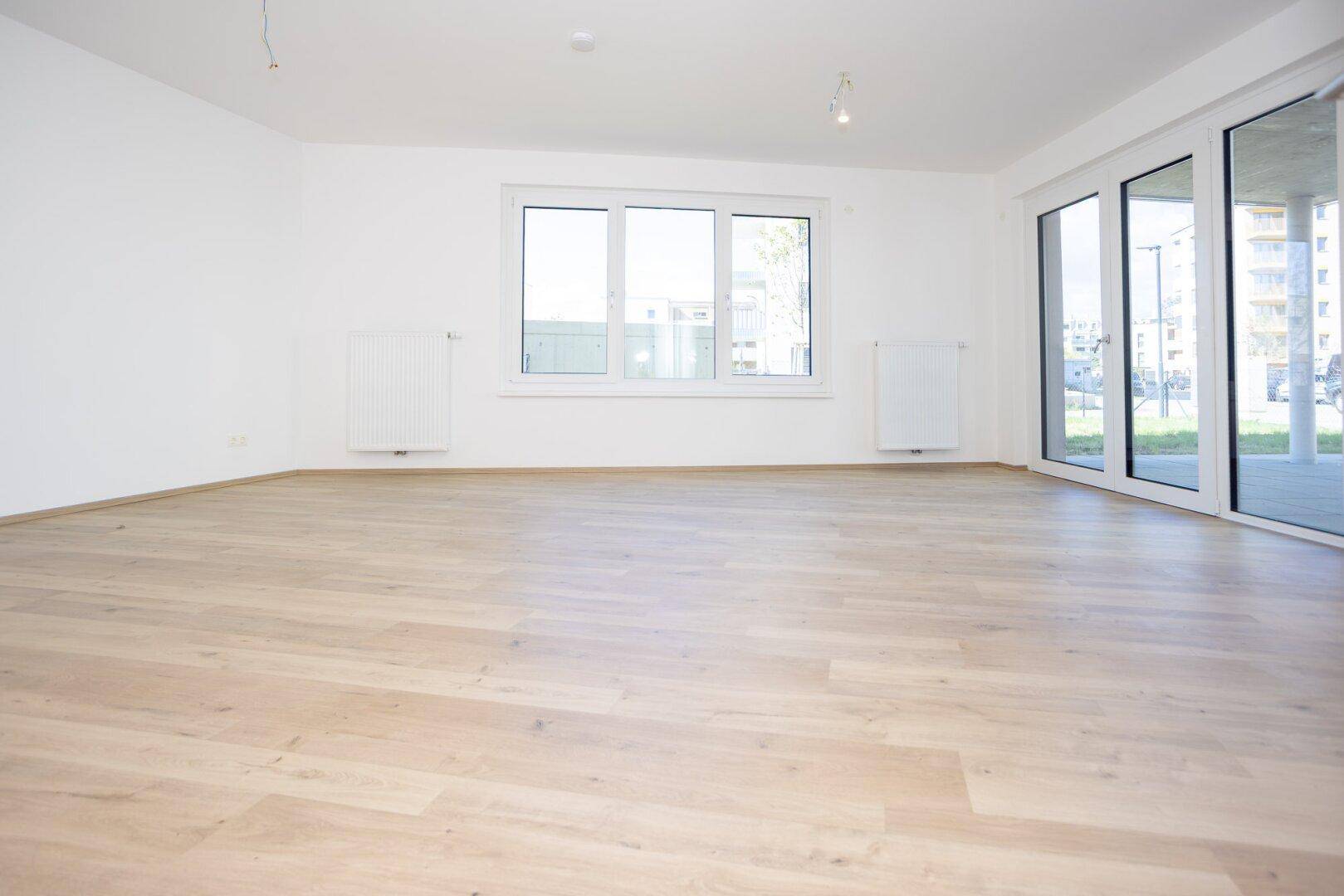 Heller, leerer Raum mit großen Fenstern und Terrassentüren, ideal für ein Wohnzimmer.
