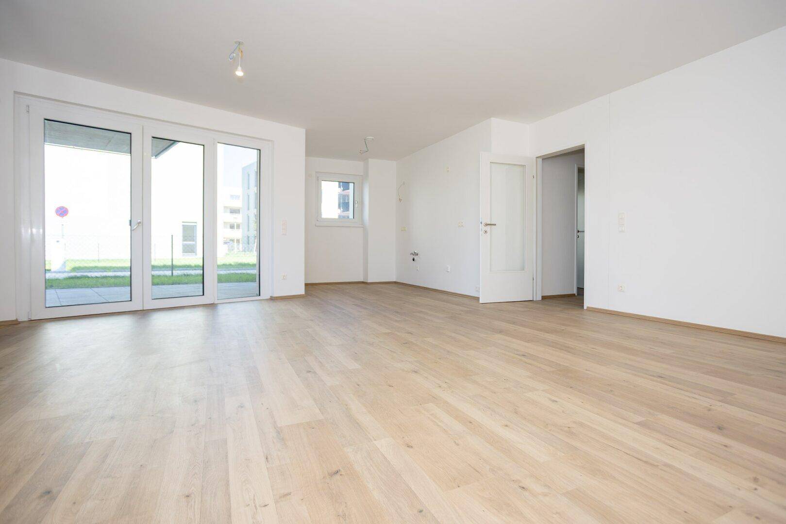 Geräumiges, helles Wohnzimmer mit Laminatboden und großen Terrassentüren, bereit zur Einrichtung.