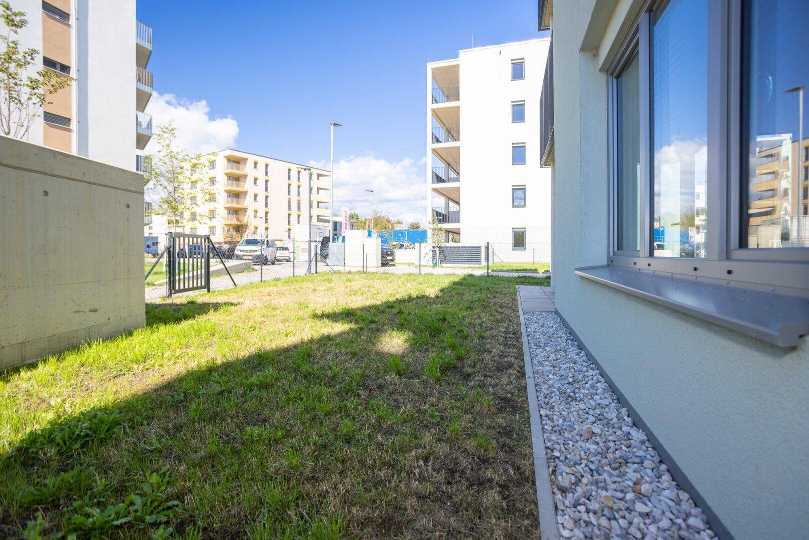 Grüne Rasenfläche neben dem Neubau mit Blick auf weitere Wohngebäude.