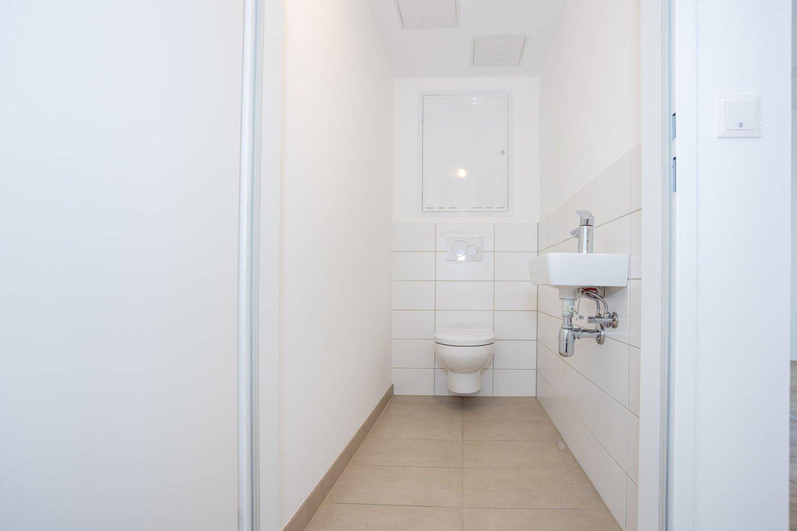 Separates Gäste-WC mit wandhängender Toilette, kleinem Waschbecken und weißen Fliesen.