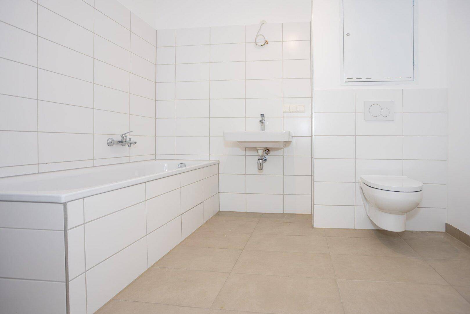 Modernes Badezimmer mit weißen Fliesen, Badewanne, Waschbecken und wandhängendem WC.