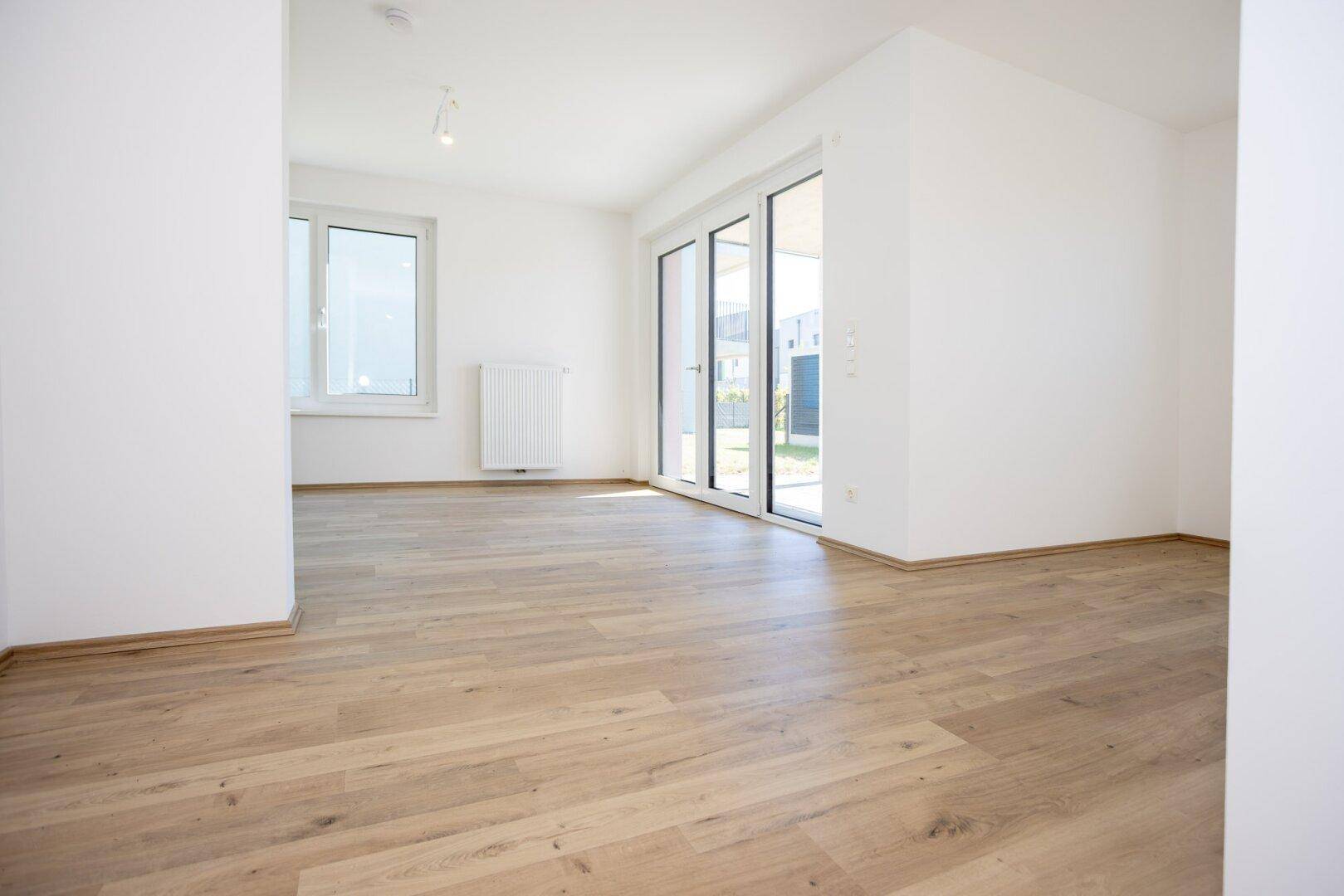 Helles, leeres Wohnzimmer mit Laminatboden und Zugang zu einer Terrasse oder Garten.