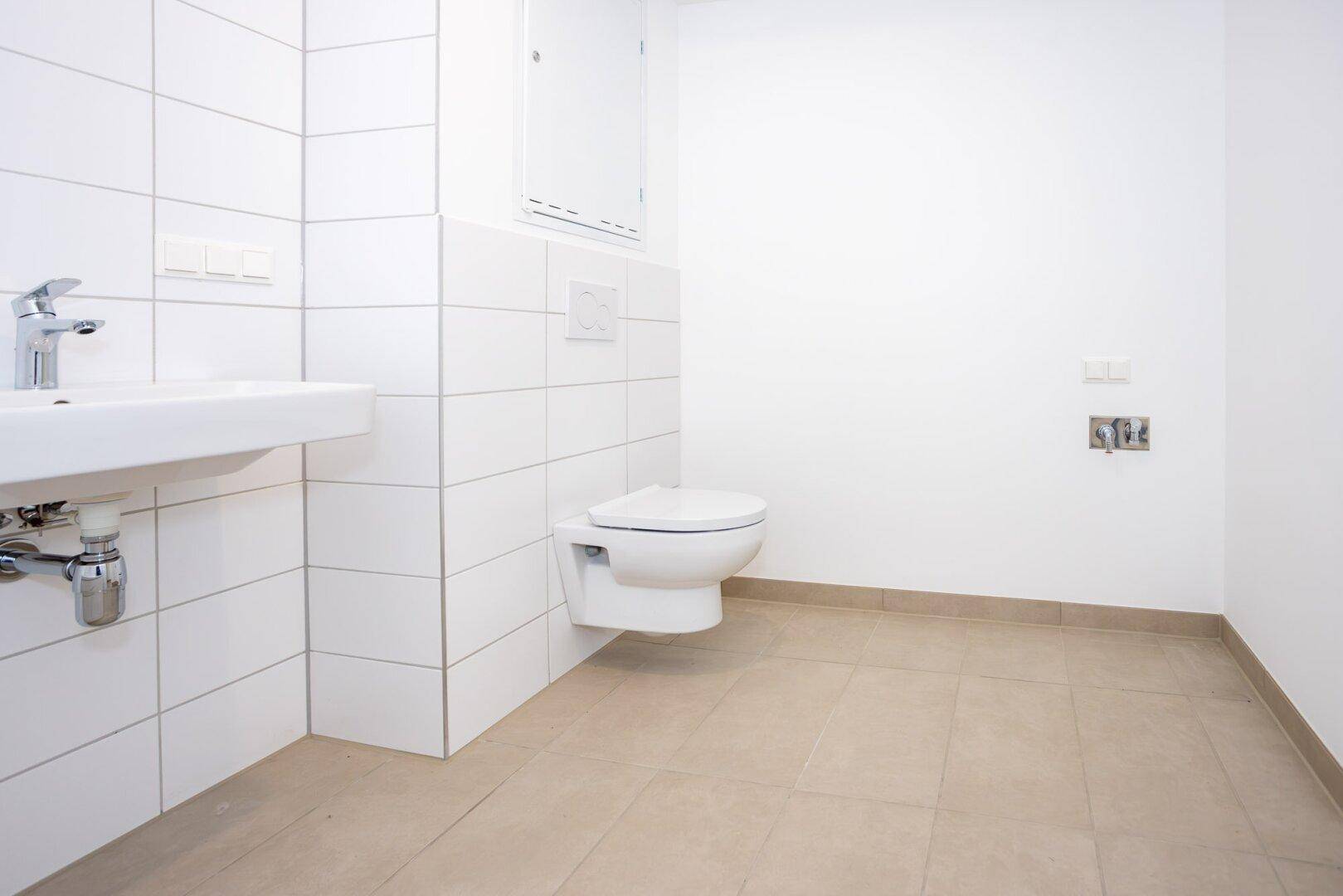 Kleines Gäste-WC mit wandhängendem WC und modernem Waschbecken, hell gefliest.