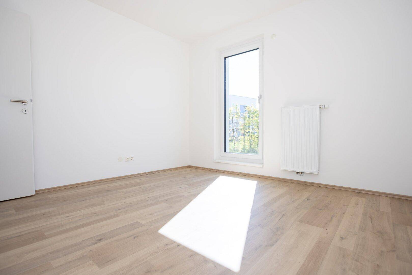 Helles Schlafzimmer mit Laminatboden und Fenster, das einen Blick ins Grüne bietet.