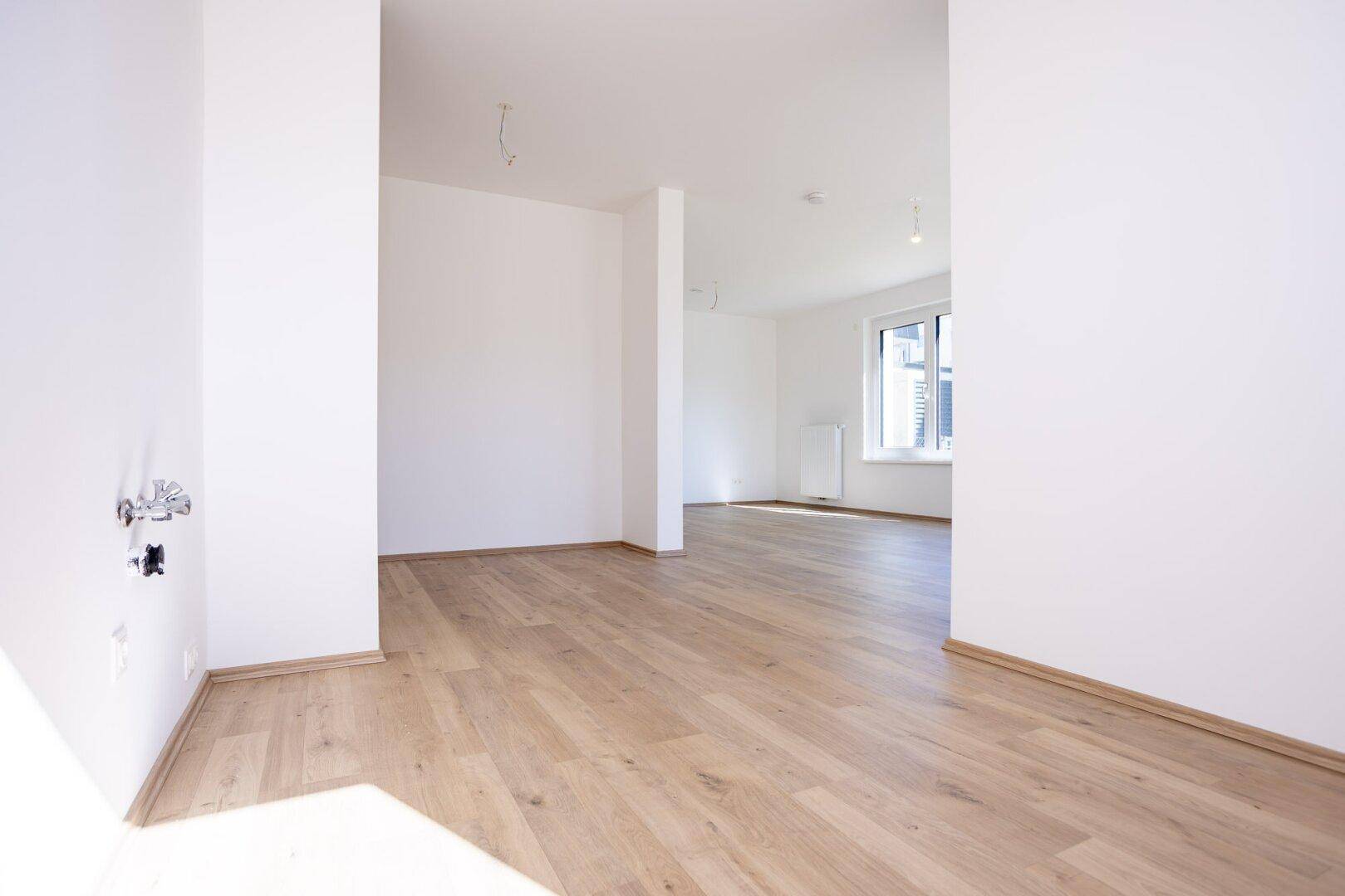 Geräumiger, heller Wohnbereich mit Laminatboden und offenem Übergang zu einem weiteren Raum.