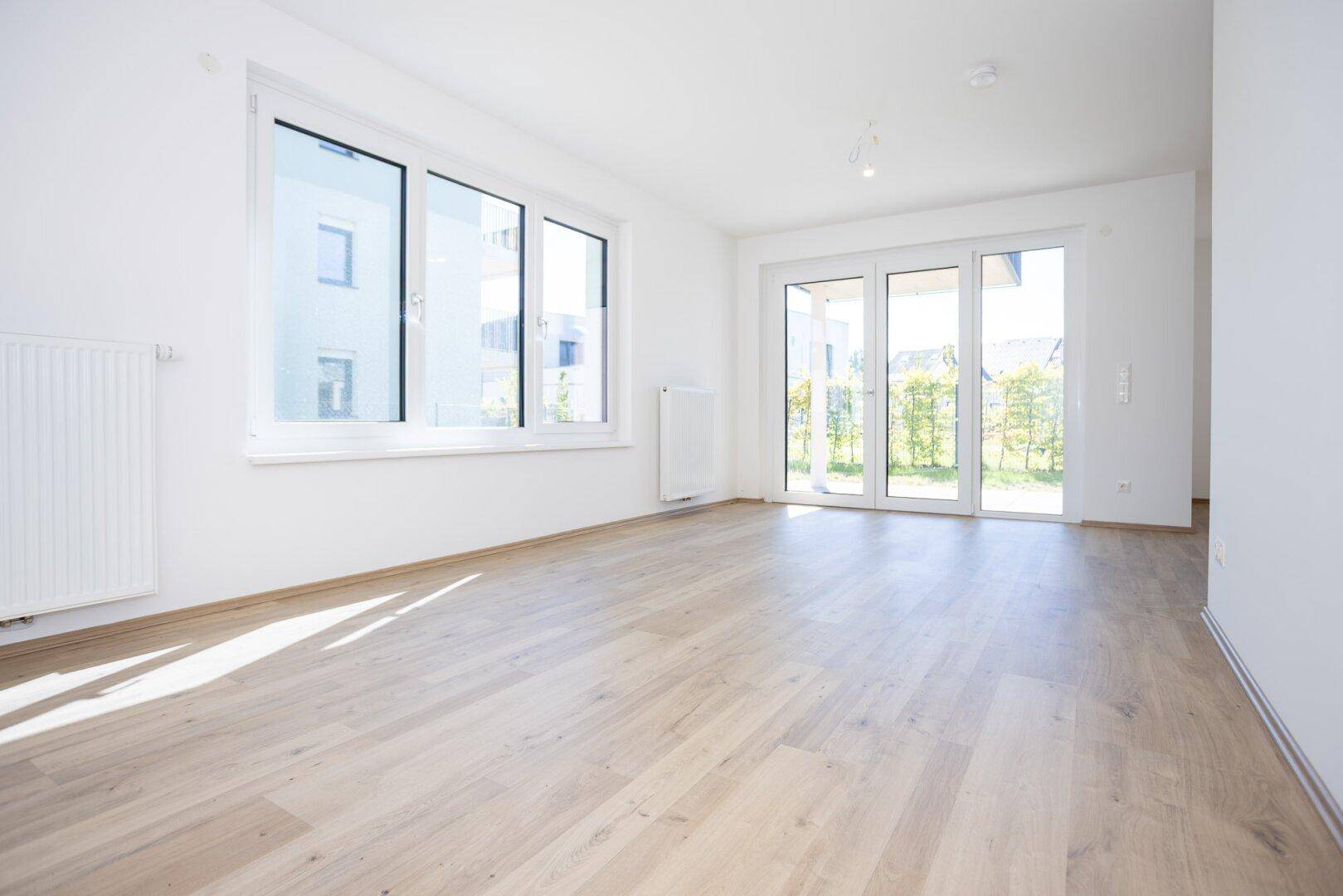 Lichtdurchfluteter Wohnbereich mit großen Fenstern, Laminatboden und Zugang zum Balkon oder Garten.