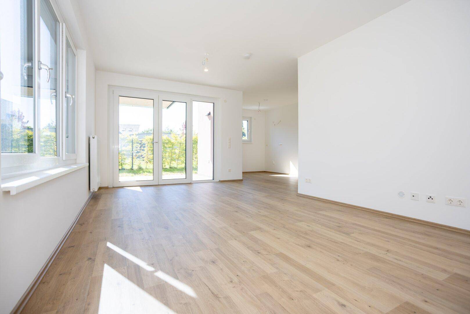 Geräumiger, heller Wohnbereich mit Laminatboden und großen Fenstern, die viel Tageslicht spenden.