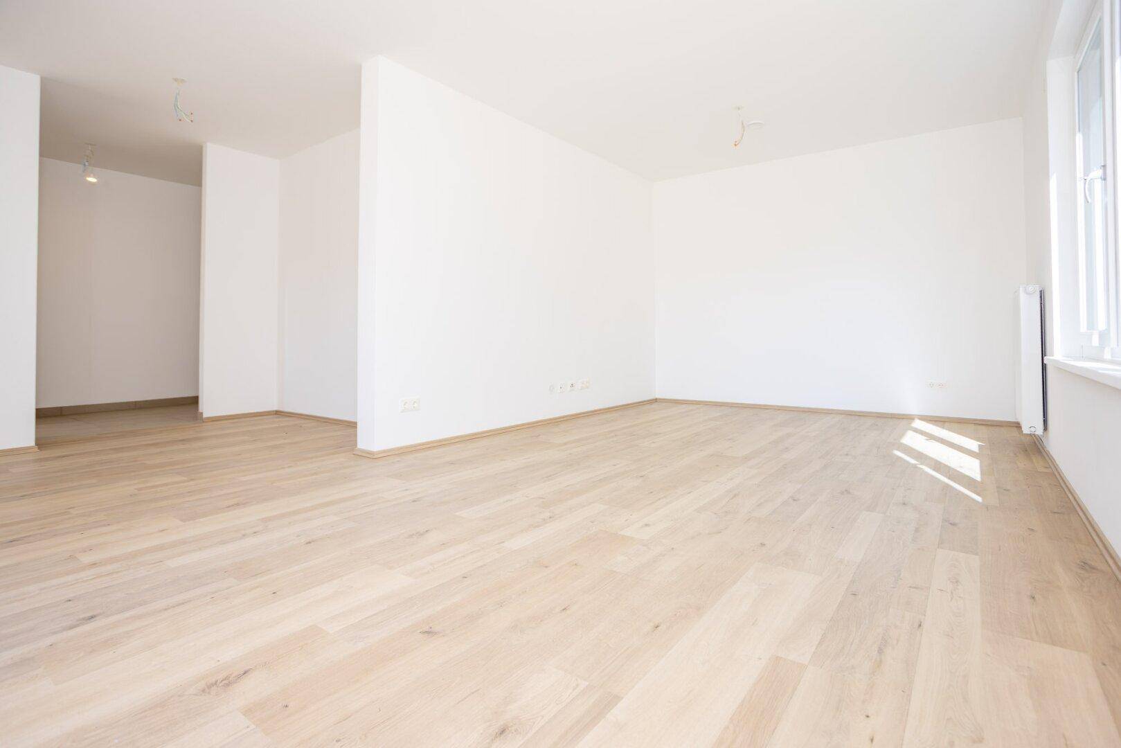 Heller, leerer Wohnbereich mit Laminatboden und weiß gestrichenen Wänden, bereit zum Einzug.
