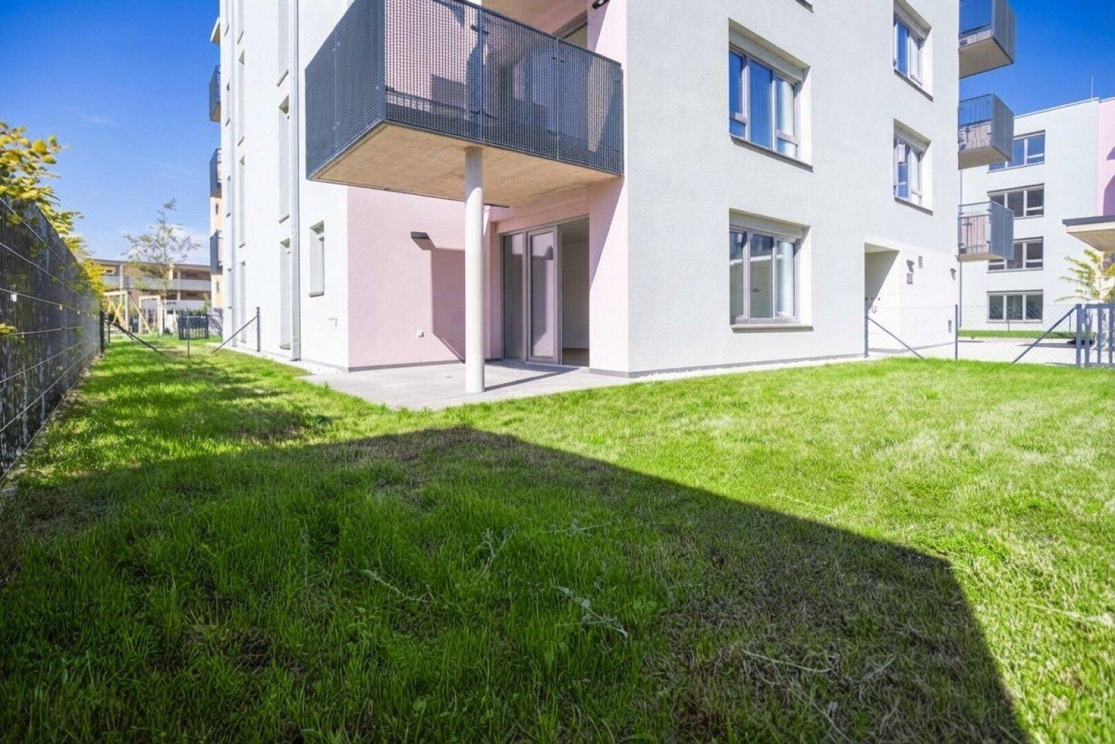 Grüne Rasenfläche neben dem Gebäude mit kleiner Terrasse und Balkon im Obergeschoss.