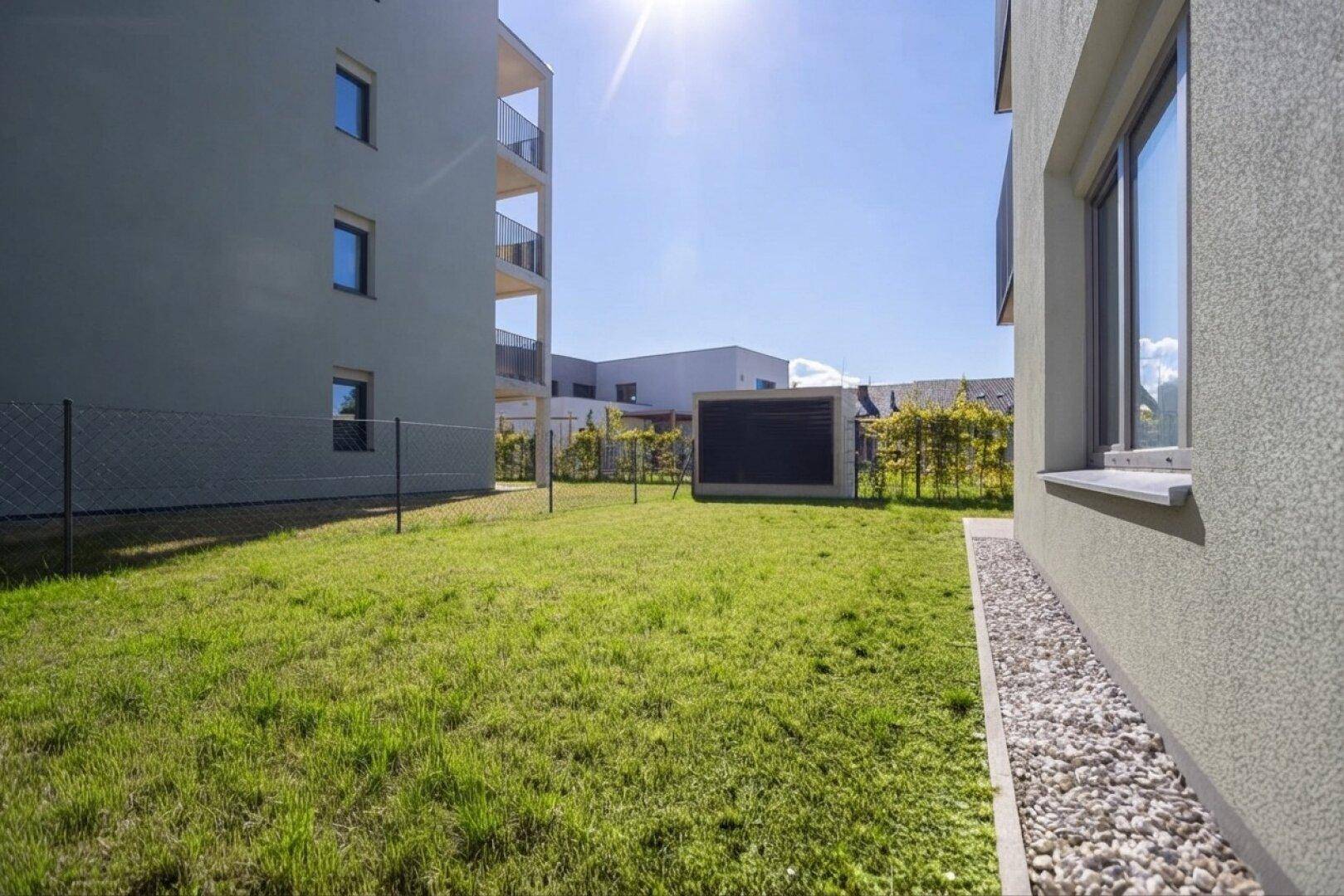 Sonnige Rasenfläche neben dem modernen Gebäude mit weiteren Wohnkomplexen im Hintergrund.