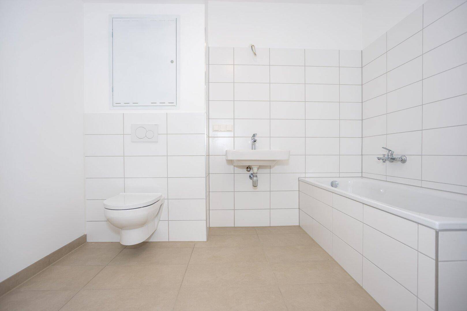 Modernes Badezimmer mit weißen Fliesen, Badewanne, Waschbecken und wandhängendem WC.
