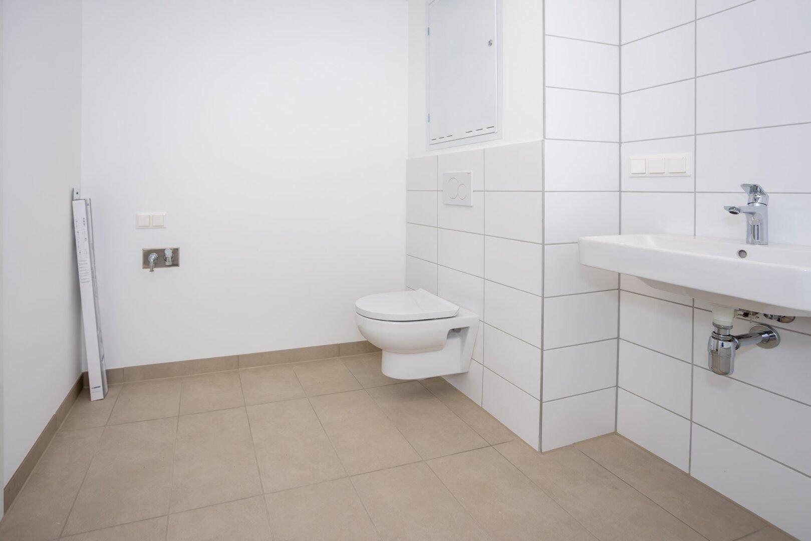 Helles Badezimmer mit weißen Wandfliesen, WC und Waschbecken, bereit zur Fertigstellung.