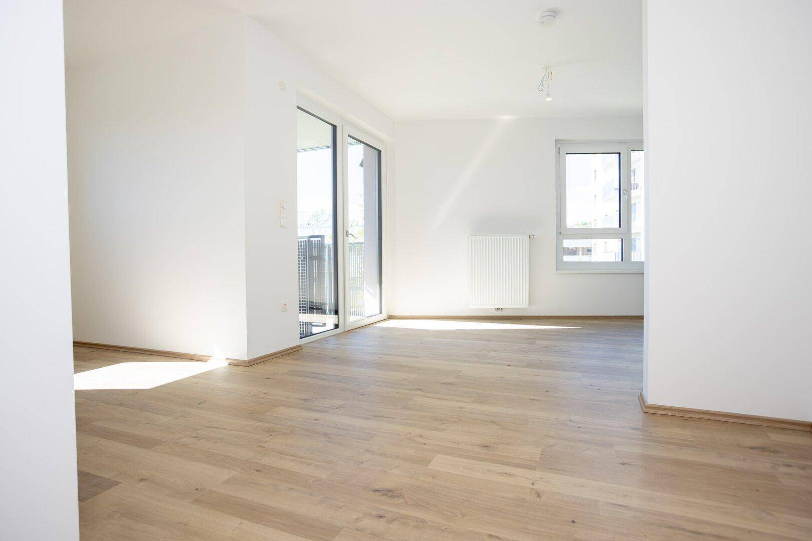 Heller, unmöblierter Wohnbereich mit großen Fenstern und Zugang zum Balkon.