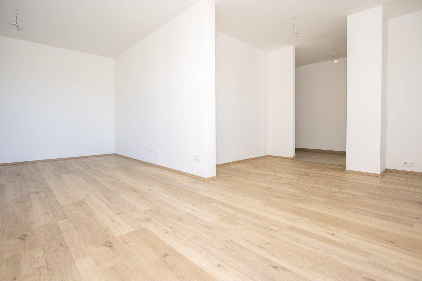 Geräumiger, leerer Raum mit hellem Laminatboden und weißen Wänden, bereit zum Einzug.