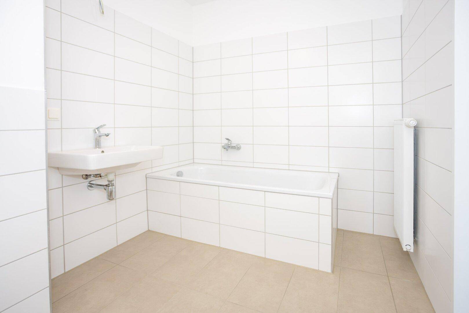 Sauberes Badezimmer mit Badewanne, Waschbecken und weißen Fliesen, unmöbliert.