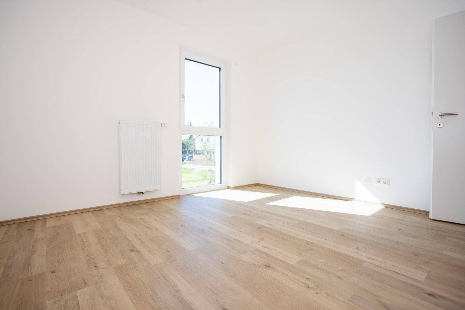 Leeres Schlafzimmer mit viel Tageslicht, Laminatboden und weiß gestrichenen Wänden.