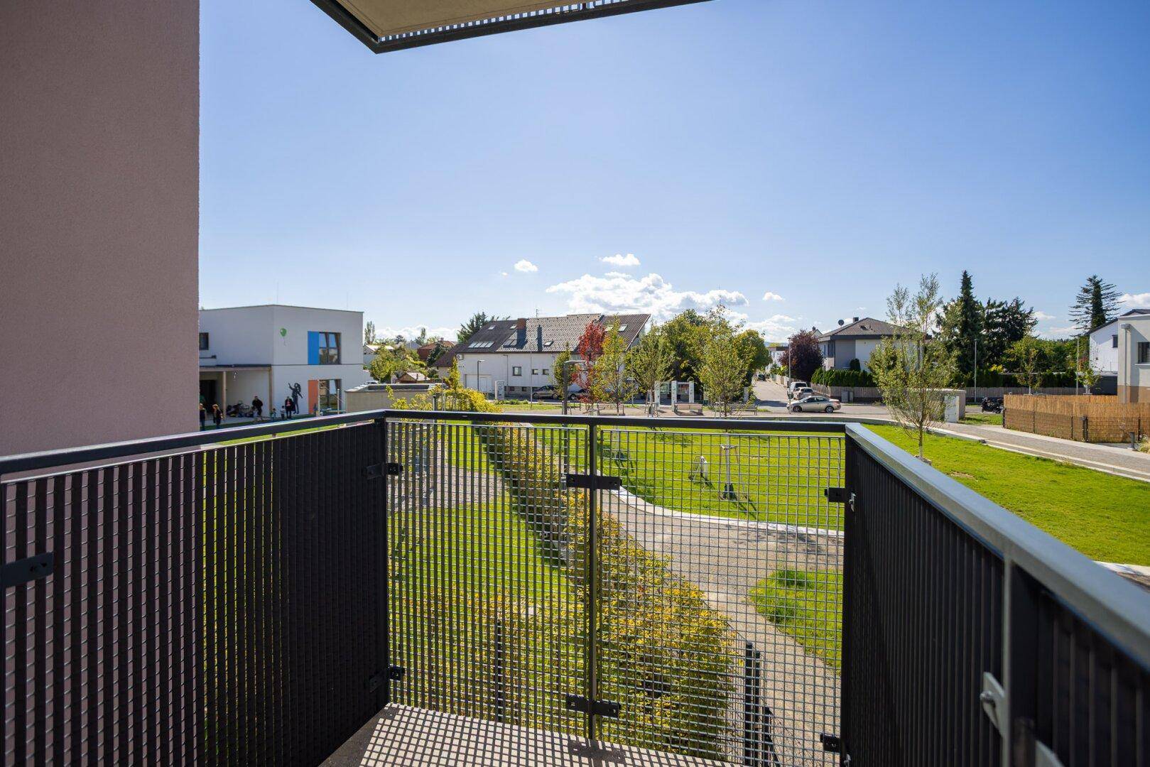 Sonniger Balkon mit Gittergeländer und weitem Blick über die Wohngegend.