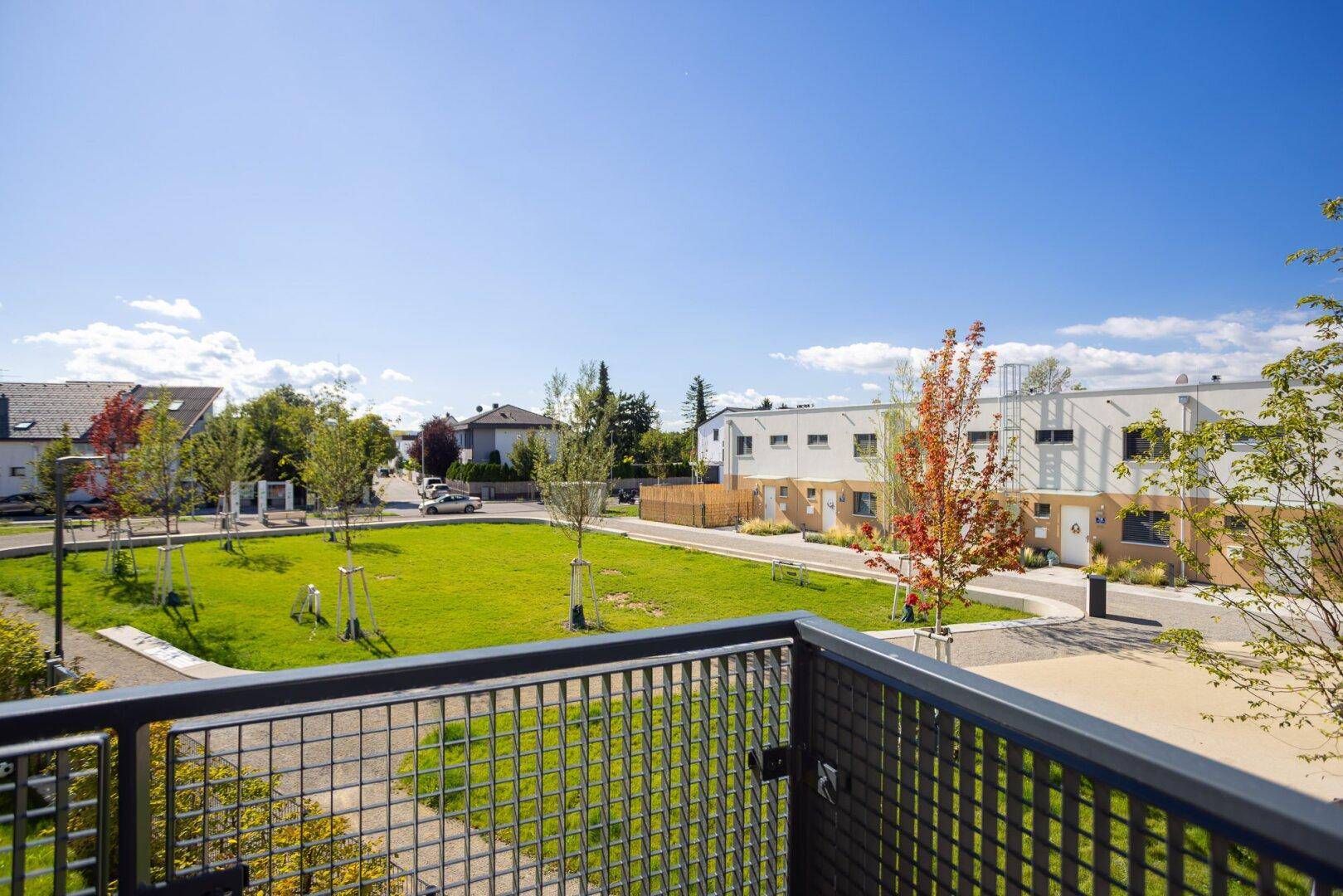 Blick vom Balkon auf eine grüne Gemeinschaftsfläche und moderne Reihenhäuser.