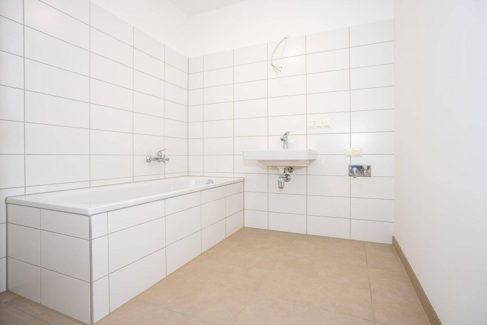 Modernes Badezimmer mit weißen Fliesen, einer Badewanne und einem Waschbecken.