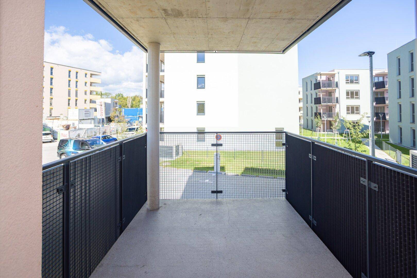 Langer Balkon mit modernem Gittergeländer und weitem Blick auf die Wohnsiedlung.
