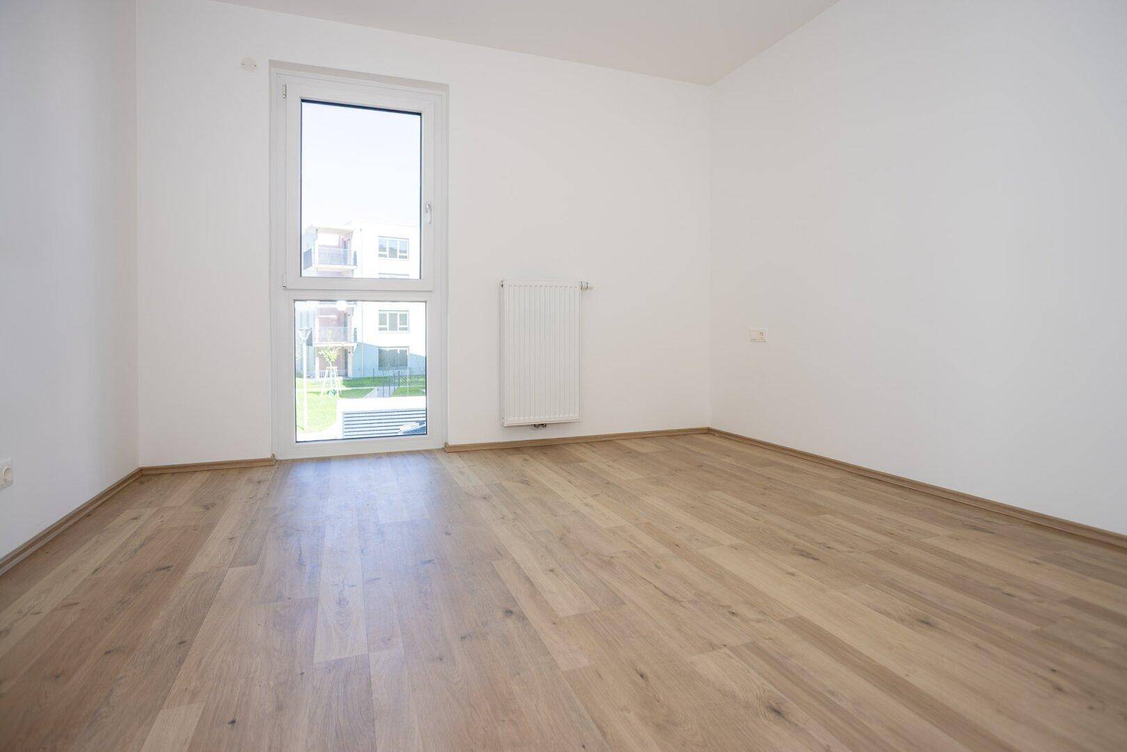 Helles Schlafzimmer mit Laminatboden, weiß gestrichenen Wänden und einem großen Fenster.